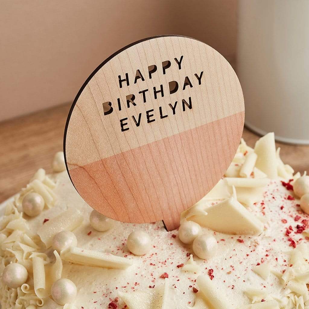 Wooden cake topper engraved 'Happy Birthday Evelyn' on a birthday cake
