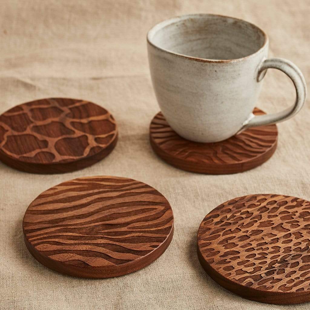 Set of four wooden coaster engraved with animal print patterns; shown on a table cloth with mug