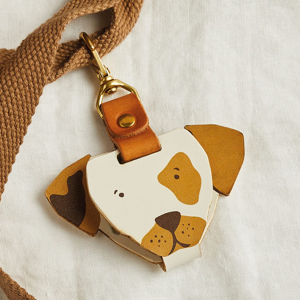 A leather bag tag in the shape of a dog with brown and white markings, attached to a school bag strap