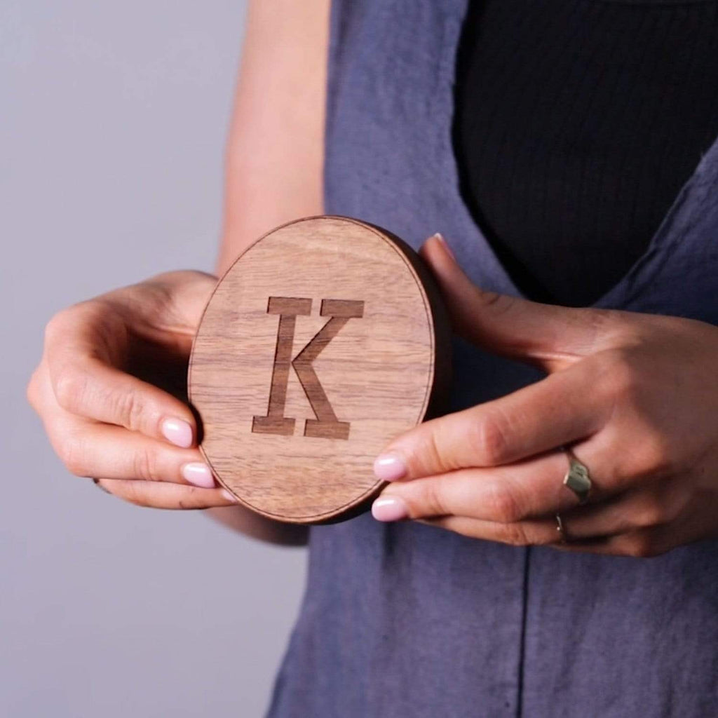 Female hand model holding a wooden coaster, engraved with the letter K